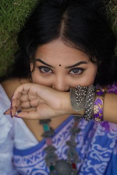 a woman with her hand on her face and bracelets around her neck, posing for the camera