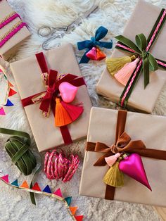 four wrapped presents with tassels and bows on them sitting on a white blanket