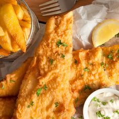 fried fish and fries are served with sour cream sauce, lemon wedges, and parsley