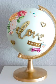 a white globe with gold lettering and flowers on the top is sitting on a stand