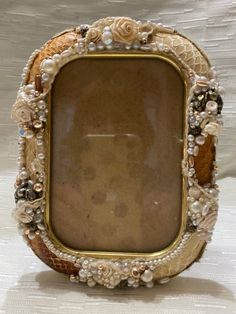 an old photo frame with pearls and flowers on the edges is sitting on a white surface