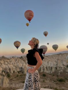 a woman standing on top of a rock next to hot air balloons