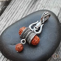 a silver and orange beaded pendant on a rock