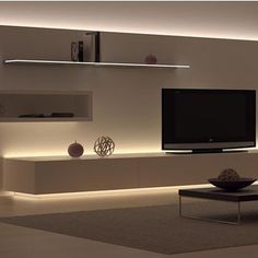 a modern living room with white walls and lights on the tv stand, coffee table and vases