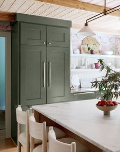 a bowl of fruit sits on the kitchen countertop next to chairs and cupboards