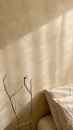 a bare tree branch in the corner of a room next to a bed with white sheets