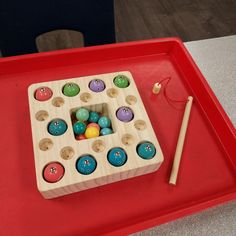 a red tray with an assortment of wooden toys on it and a pair of chopsticks next to it