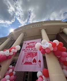 an arch decorated with pink, white and red balloons in front of a large building