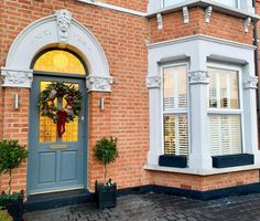 a blue front door with a wreath on it and two windows in the wall behind it