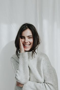 a smiling woman with her hand on her face and wearing a gray turtle neck sweater