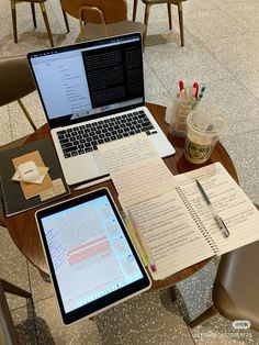 an open laptop computer sitting on top of a wooden table next to a notebook and pen