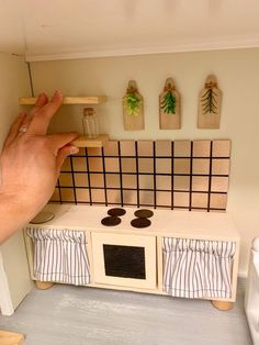 a hand is holding a piece of wood near a miniature stove top oven and wall decorations