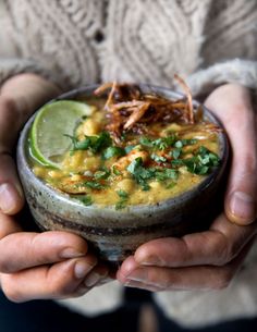 two hands holding a bowl filled with soup and garnished with cilantro