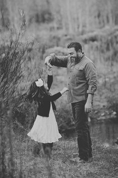 a father and daughter holding hands while walking through the woods in their black and white photo