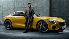 a man standing next to a yellow sports car in front of a concrete wall,