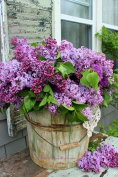 a bucket filled with purple flowers next to a window