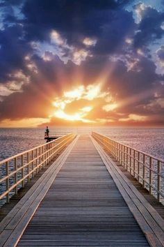 a pier with the sun setting over the water and clouds in the sky above it