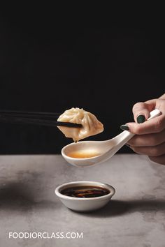 a person holding chopsticks and dipping sauce into a bowl with dumplings in it