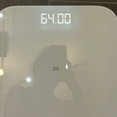 a person taking a photo with their cell phone in front of a digital scale that reads 6 00