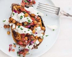 a white plate topped with an open face sandwich covered in chickpeas and sour cream