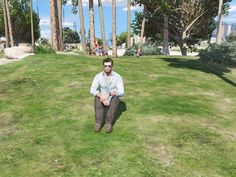 a man sitting on top of a lush green field next to tall palm tree's