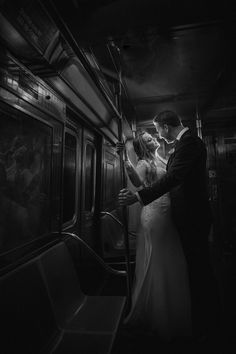 a bride and groom kissing on a subway train in black and white, with the light coming from behind them