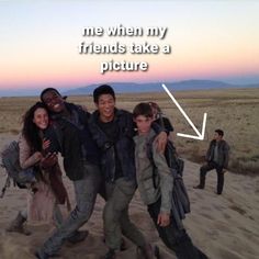 four people standing in the sand with one person pointing at the camera and another smiling