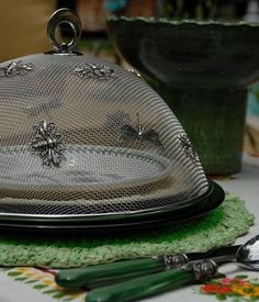 a glass covered dish sitting on top of a table next to green utensils