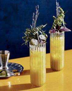 two tall vases filled with flowers on top of a yellow table next to a silver cup