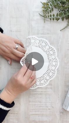 a woman is cutting paper with scissors on a table next to a laptop and flowers