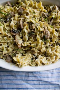 a white bowl filled with pasta and meat on top of a blue striped table cloth