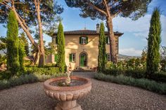 a large house surrounded by trees and bushes with a fountain in the front yard area