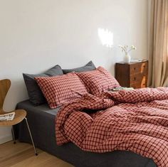 a bed with red and black checkered comforter in a white room next to a window