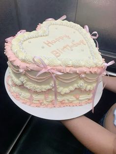 a heart shaped cake is being held up by someone's hand with pink ribbon