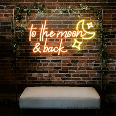 a neon sign that says to the moon and back on a brick wall behind a bench