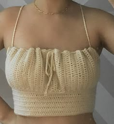 a woman wearing a beige crop top and gold chain necklace, with her hands on her hips