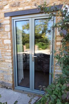 Gorgeous traditional style aluminum double glazed french doors in a heritage green, set in a pale stone wall, with a vale of foliage draping down one side. Glass reflecting a sunny sky, luscious green trees and a gravel drive way. French Door With Shutters, Aluminium French Doors White, Green Aluminium Windows, Aluminium French Doors Exterior, Small French Doors Exterior, Green French Doors, Cottage Scotland, External Glass Doors, Narrow French Doors