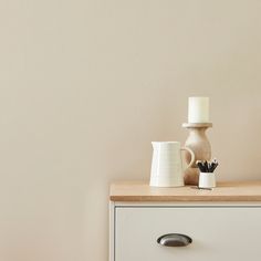 two white vases sitting on top of a dresser next to a cup and brush