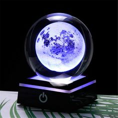 a glass ball with blue flowers on it sitting on top of a wooden stand in front of a black background