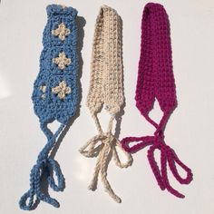 three crocheted headbands are lined up on a white surface, one is blue and the other is pink