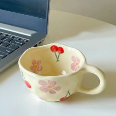 a coffee cup sitting next to a laptop computer on a white table with flowers painted on it