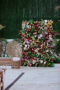 a chair sitting in front of a flower covered wall next to a wicker chair