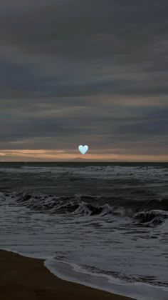 a heart - shaped object floating in the air over an ocean with waves and dark clouds