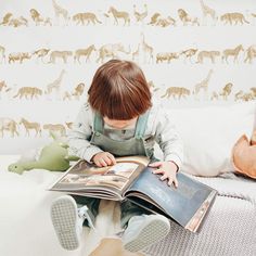 a little boy sitting on top of a bed reading a book