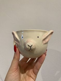 a hand holding a white ceramic pig bowl with red nails on it's fingers