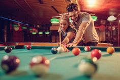 a man and girl playing pool together in a room with many balls on the table