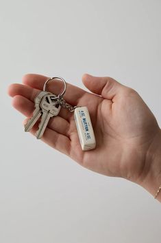 a hand holding a small key chain with two keys attached to it, in front of a white background