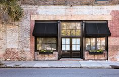 an old brick building with black awnings and palm trees on the sidewalk in front