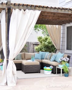 an outdoor living area with couches, pillows and curtains on the side of the house