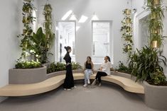 three women are sitting on a bench in the middle of a room filled with plants